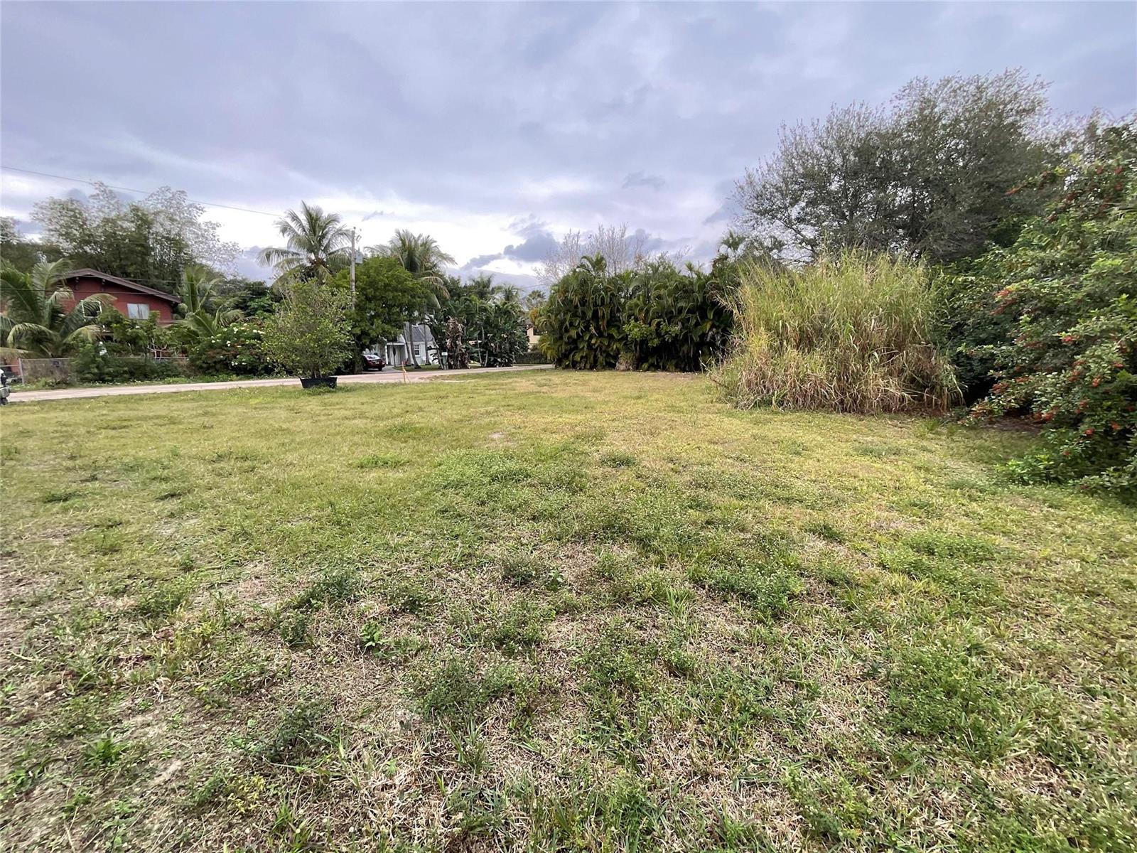 An empty, grassy residential lot with surrounding trees and shrubs under a cloudy sky — 6650 Riggers Road, Lake Worth FL 33462, LAKE WORTH, FL