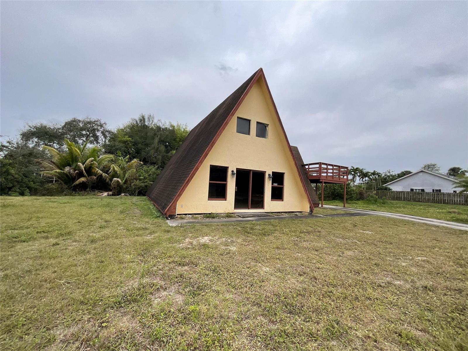 A yellow A-frame house stands on a grassy lot with an attached wooden deck — 6650 Riggers Road, Lake Worth FL 33462, LAKE WORTH, FL