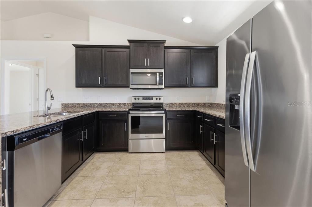 A kitchen features dark wood cabinets, stainless steel appliances, and granite countertops — 191 W PINE VALLEY LANE, ROTONDA WEST, FL