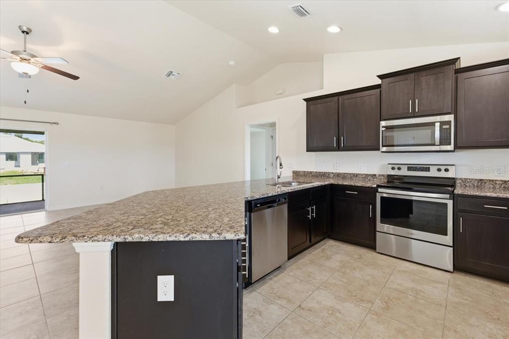 A kitchen features dark wood cabinets, granite countertops, stainless steel appliances, and tile flooring — 191 W PINE VALLEY LANE, ROTONDA WEST, FL