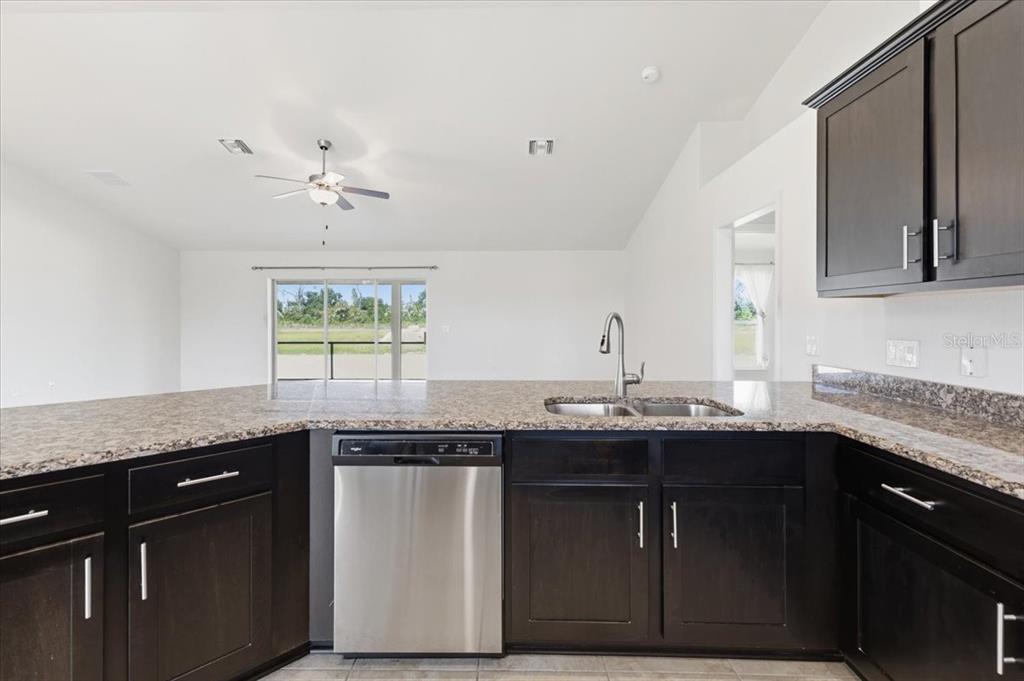 A kitchen with dark cabinets, granite countertops, and a stainless steel dishwasher overlooks a living area — 191 W PINE VALLEY LANE, ROTONDA WEST, FL