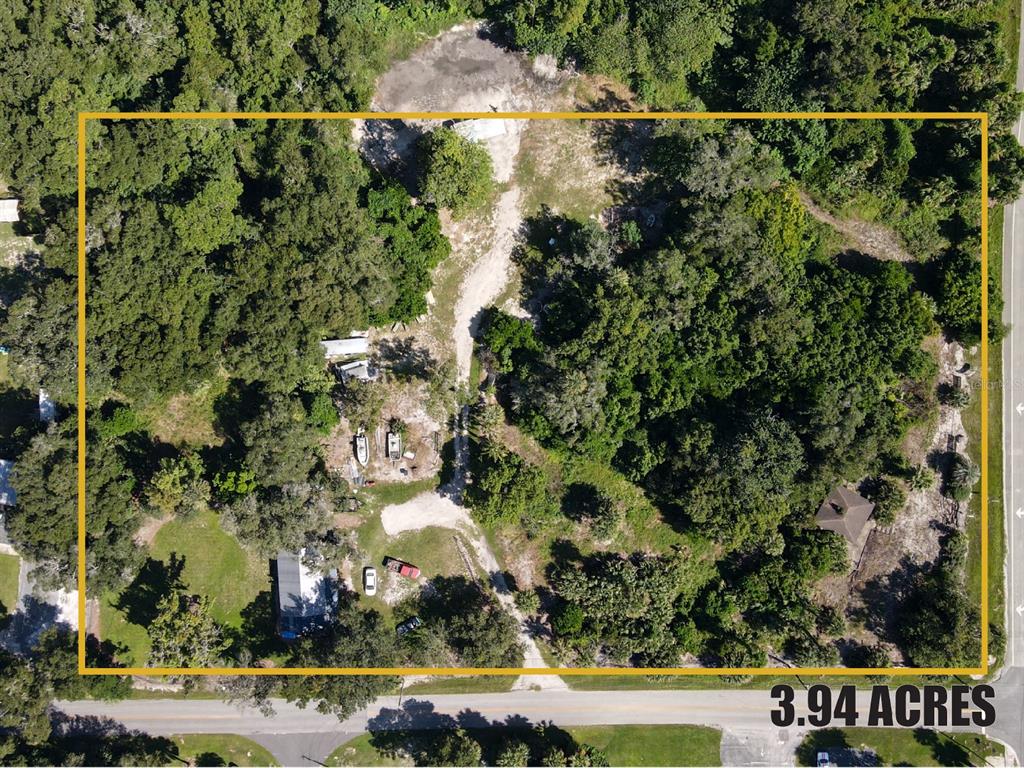 An aerial view shows a rectangular 3.94-acre wooded lot with a dirt driveway and structures — 235 W WISCONSIN AVENUE, ORANGE CITY, FL