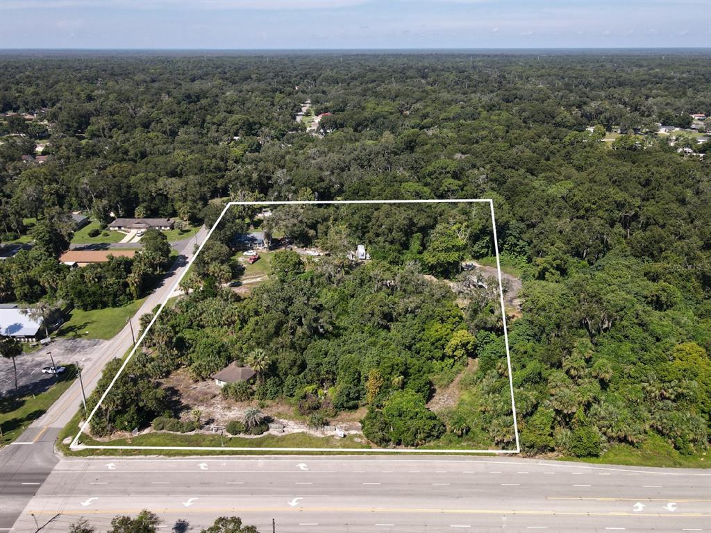 An aerial view shows a large, wooded lot outlined in white next to a paved road — 235 W WISCONSIN AVENUE, ORANGE CITY, FL