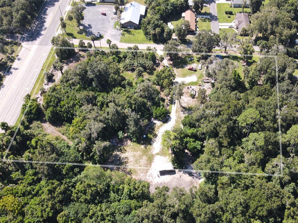 An aerial view shows a wooded lot with a dirt driveway and a small structure — 235 W WISCONSIN AVENUE, ORANGE CITY, FL