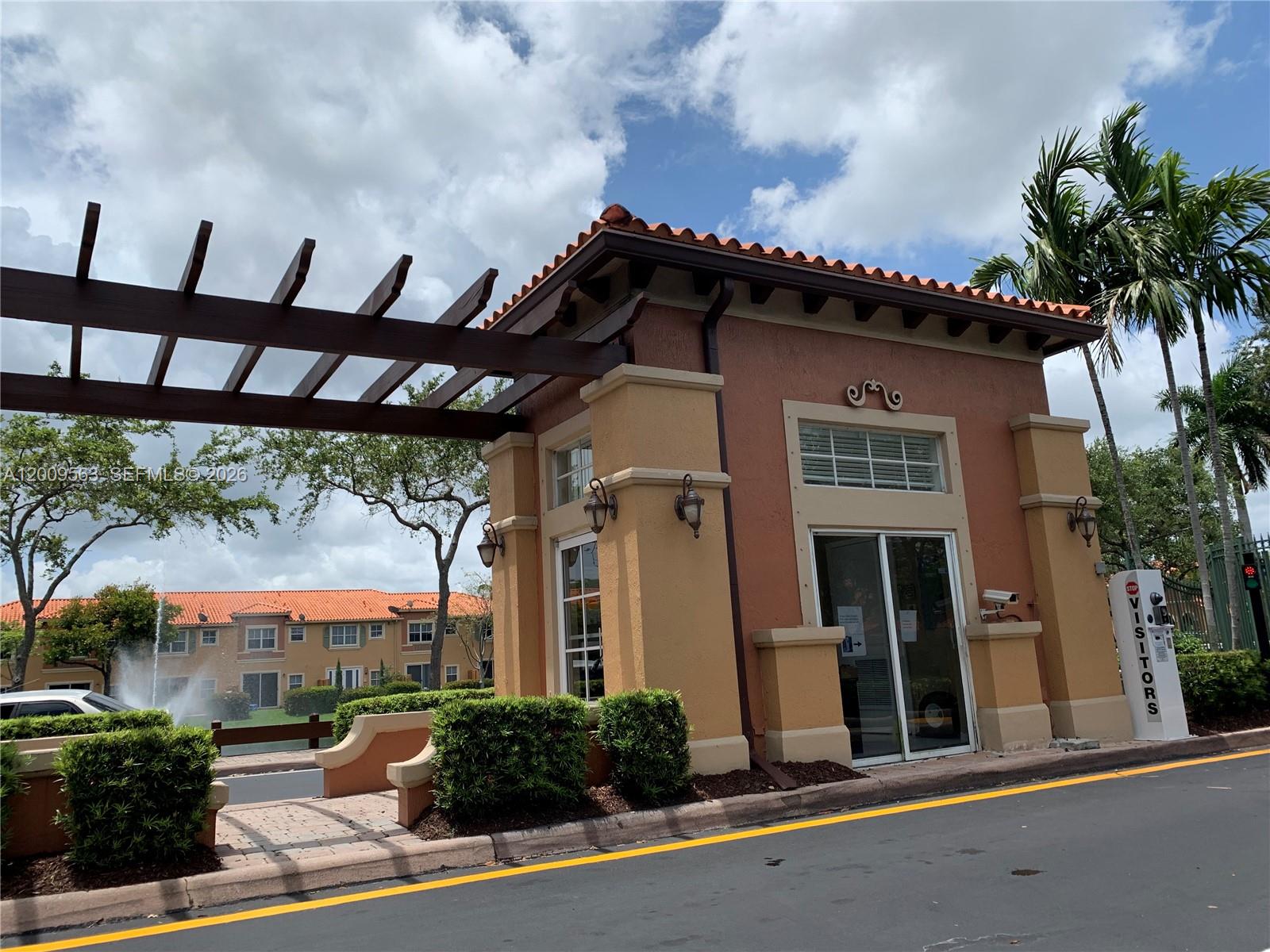A gated community entrance features a stucco guardhouse with a wooden pergola and palm trees — 4944 Windward Way # 1401, Dania Beach FL 33312, DANIA BEACH, FL