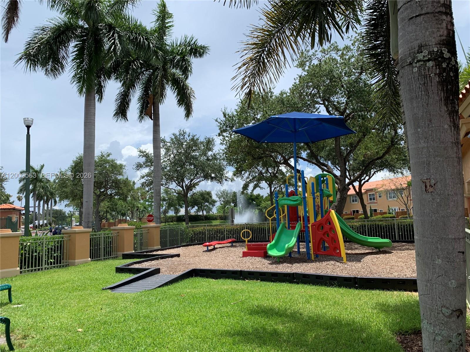 A playground with a blue umbrella, slides, and climbing equipment sits on wood chips — 4944 Windward Way # 1401, Dania Beach FL 33312, DANIA BEACH, FL