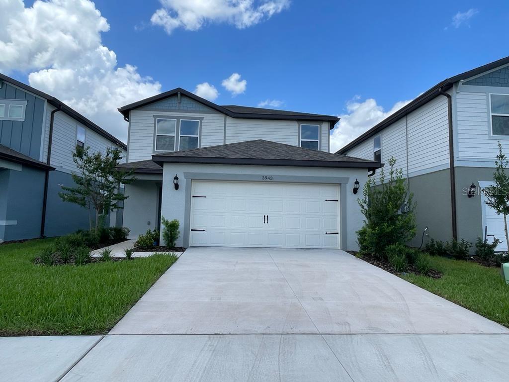 A two-story suburban house features a light gray exterior, a two-car garage, and a driveway — 3943 ALMOND BROOK BOULEVARD, LAND O LAKES, FL