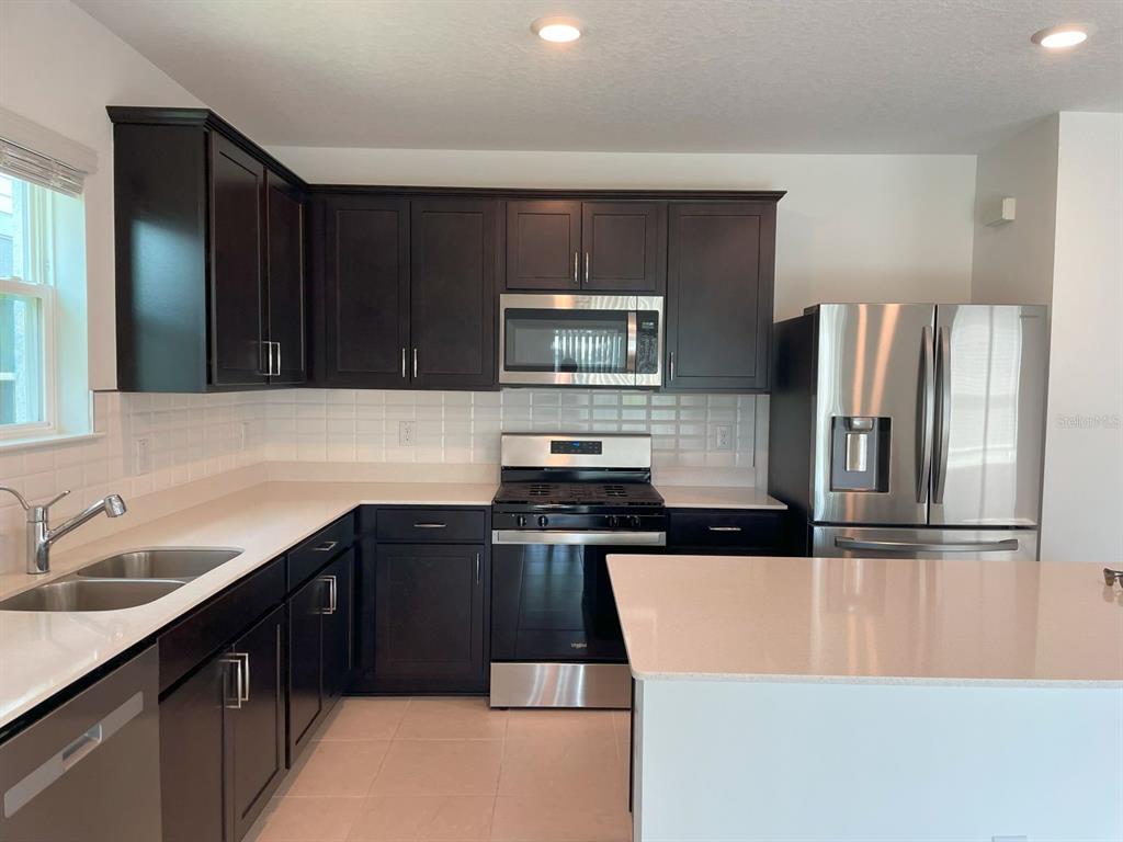 A kitchen features dark wood cabinets, stainless steel appliances, and a white quartz island — 3943 ALMOND BROOK BOULEVARD, LAND O LAKES, FL