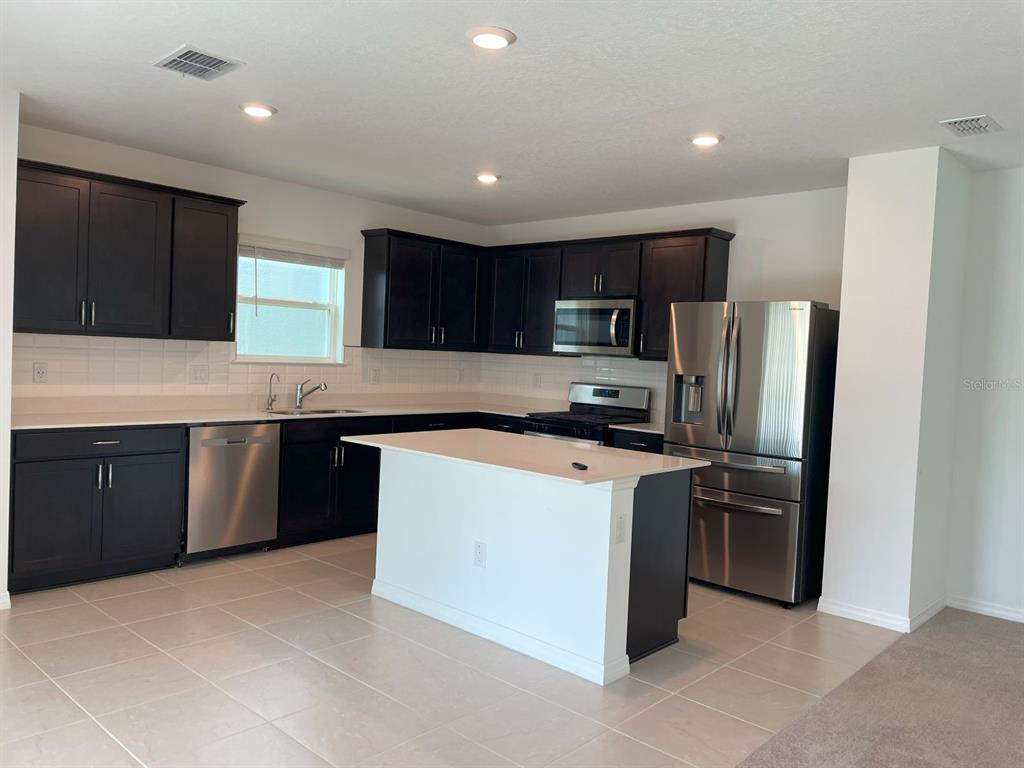 A kitchen features dark cabinets, stainless steel appliances, a white island, and light tile flooring — 3943 ALMOND BROOK BOULEVARD, LAND O LAKES, FL