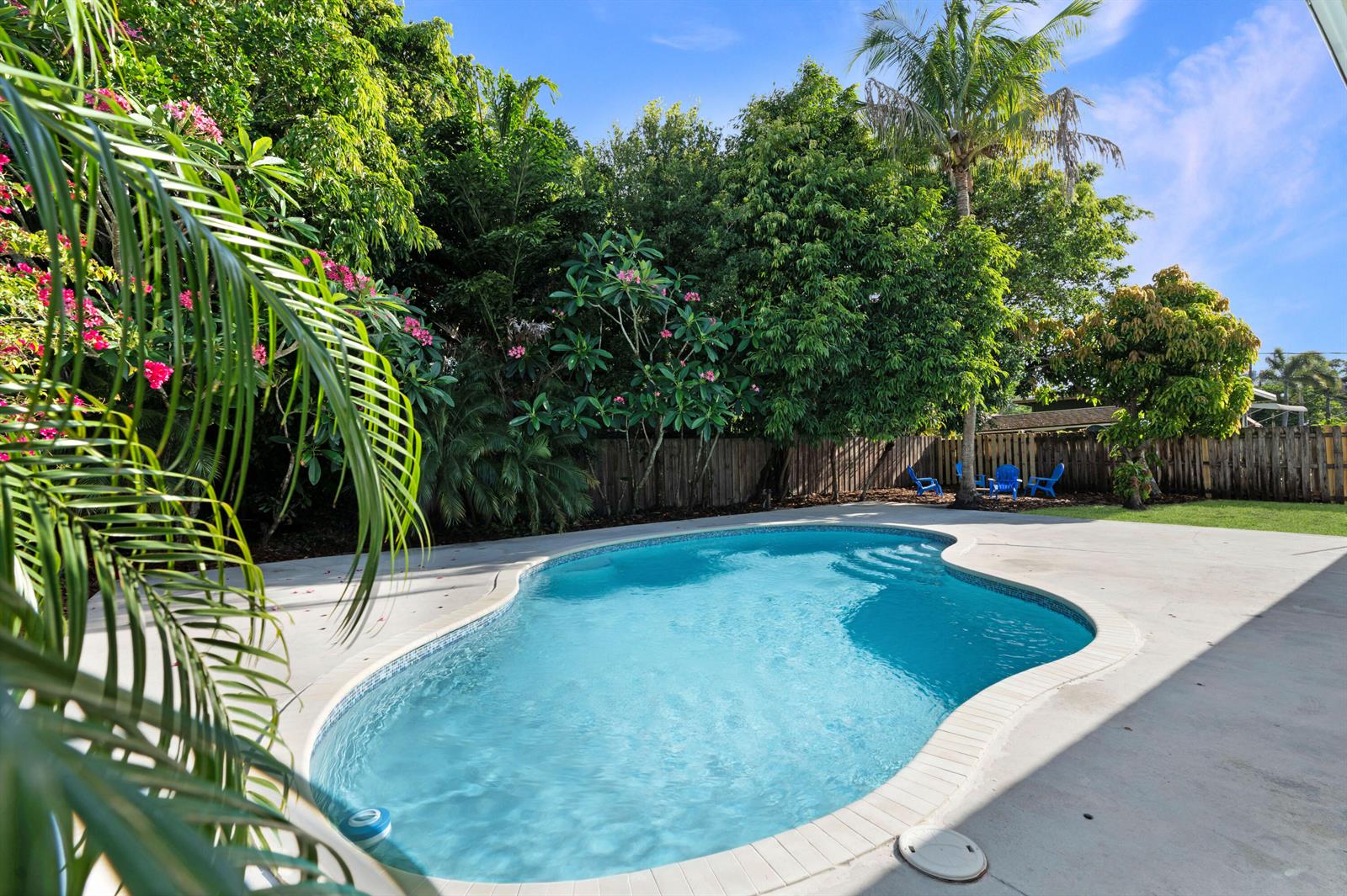 A backyard features a kidney-shaped swimming pool surrounded by a concrete patio and lush trees — 7416 Overlook Drive, Lake Worth FL 33467, LAKE WORTH, FL