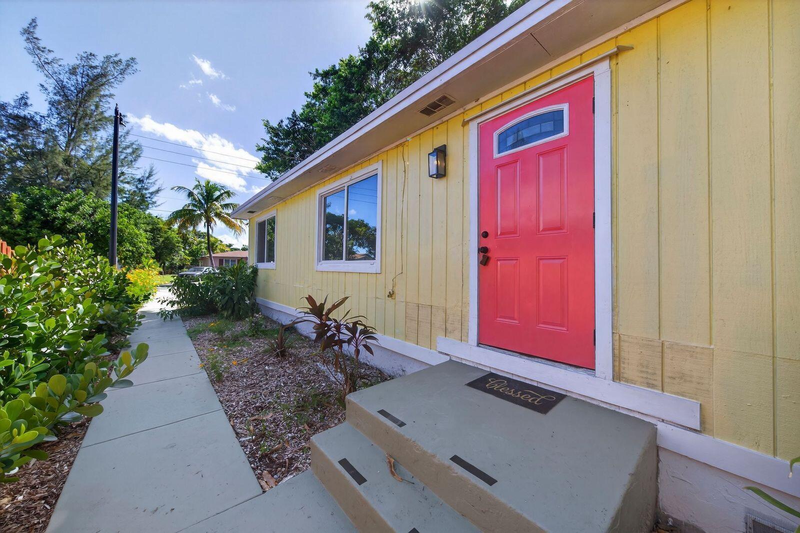 A yellow house exterior features a bright pink front door and concrete steps — 117 NE 8th Street, Pompano Beach FL 33060, POMPANO BEACH, FL