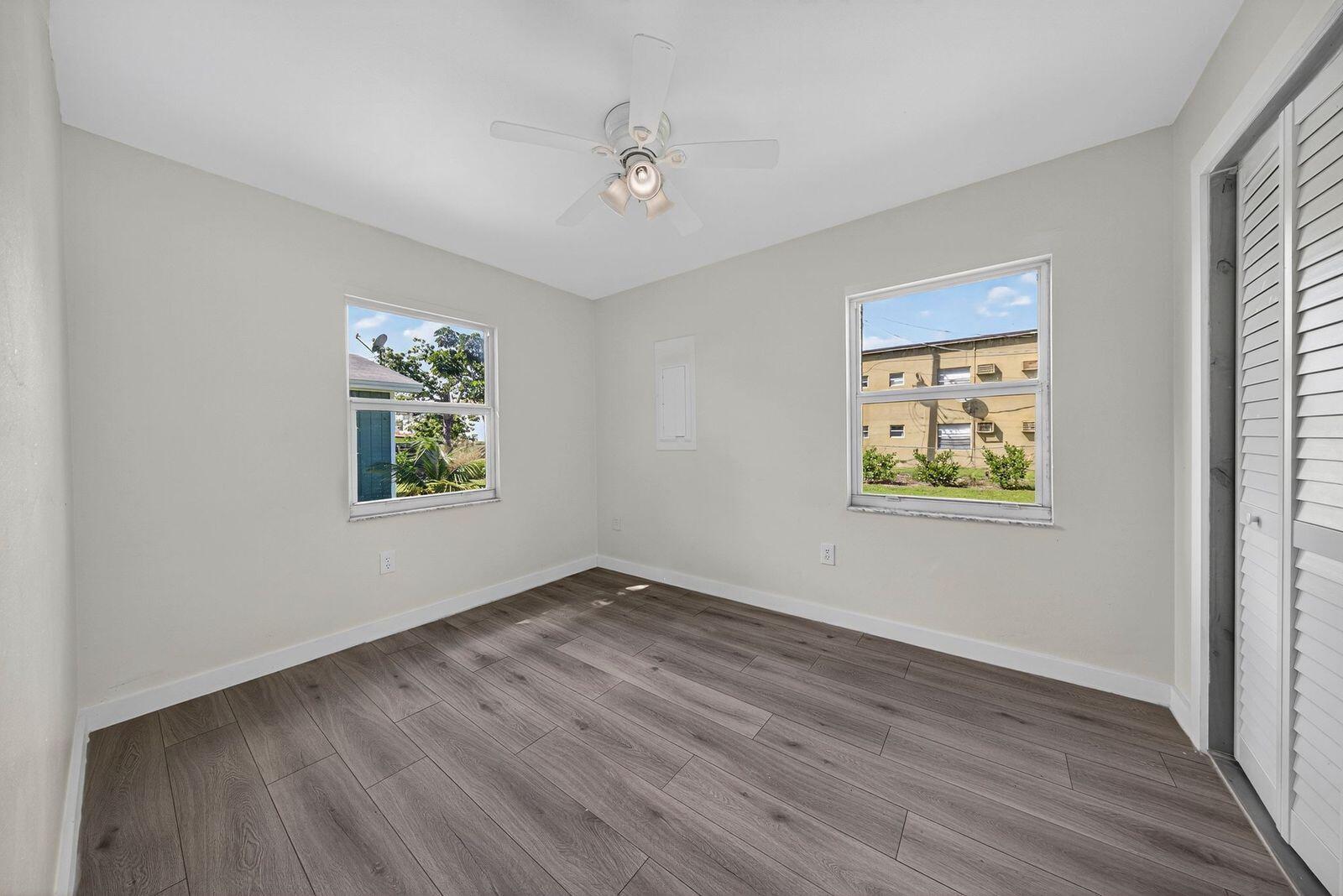An empty bedroom features light-colored walls, wood-look flooring, a ceiling fan, and two windows — 117 NE 8th Street, Pompano Beach FL 33060, POMPANO BEACH, FL