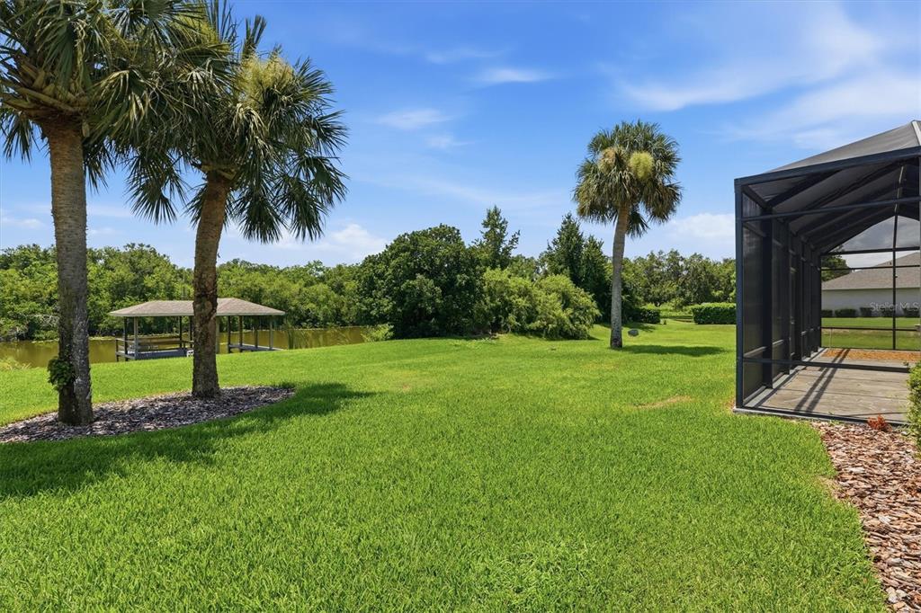 A grassy backyard features palm trees, a small dock on a pond, and a screened enclosure — 6042 LANDINGS BOULEVARD, LADY LAKE, FL