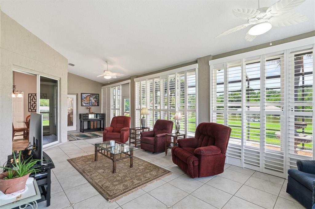 A sunroom with tile floors, three red recliners, and large windows with white plantation shutters — 6042 LANDINGS BOULEVARD, LADY LAKE, FL