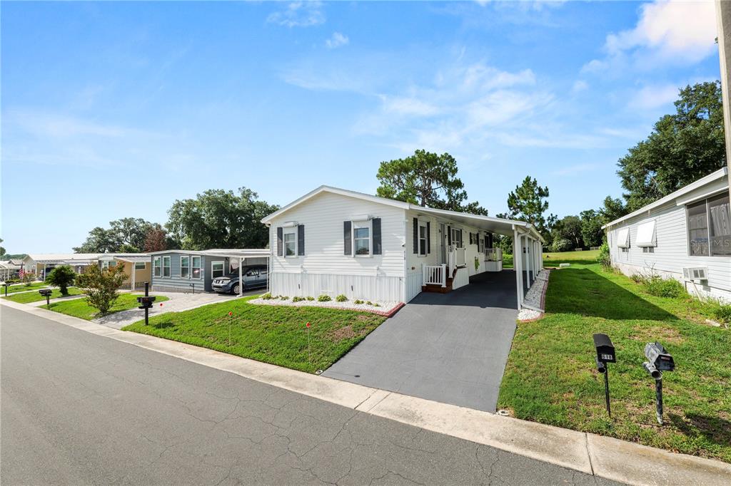 A white manufactured home with a carport and driveway sits on a grassy residential street — 618 CASSANDRA LANE, LAKELAND, FL