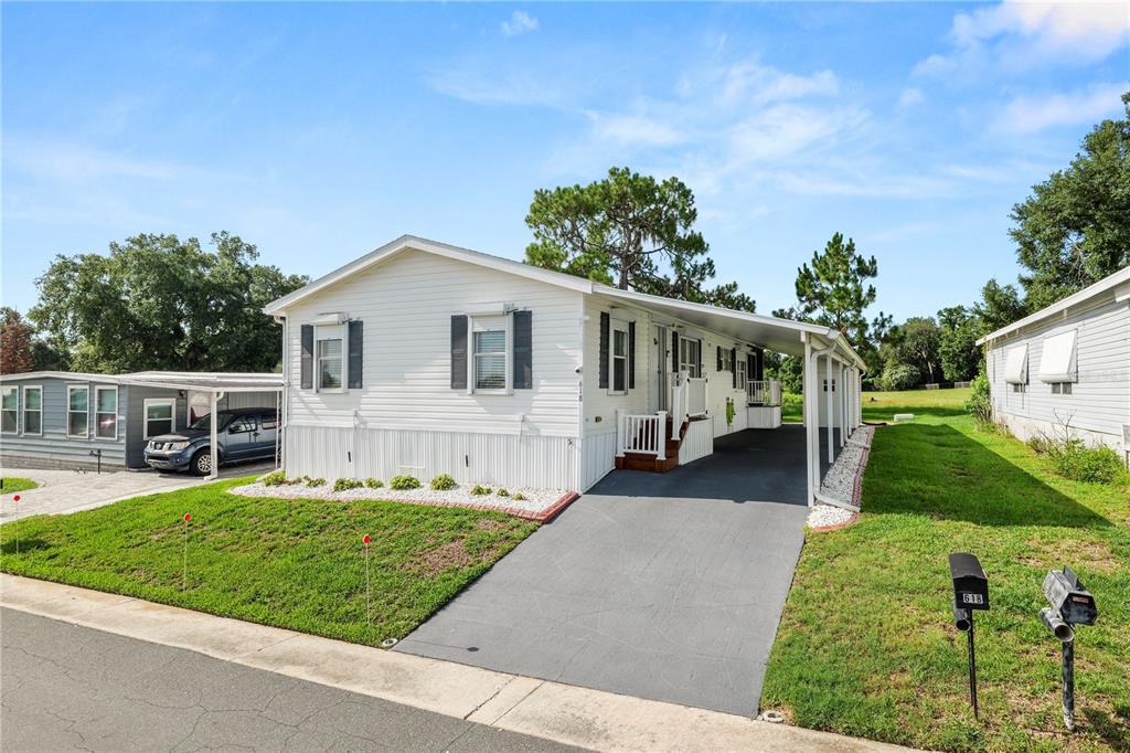 A white manufactured home with a carport, driveway, and lawn under a blue sky — 618 CASSANDRA LANE, LAKELAND, FL