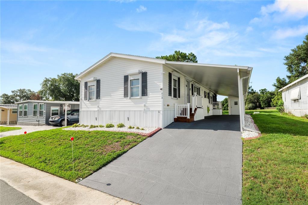 A white manufactured home features a gray driveway, a carport, and a small front lawn — 618 CASSANDRA LANE, LAKELAND, FL