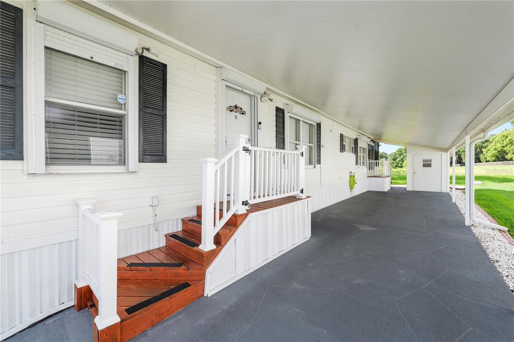 A white mobile home exterior features a covered concrete patio and wooden stairs with railings — 618 CASSANDRA LANE, LAKELAND, FL