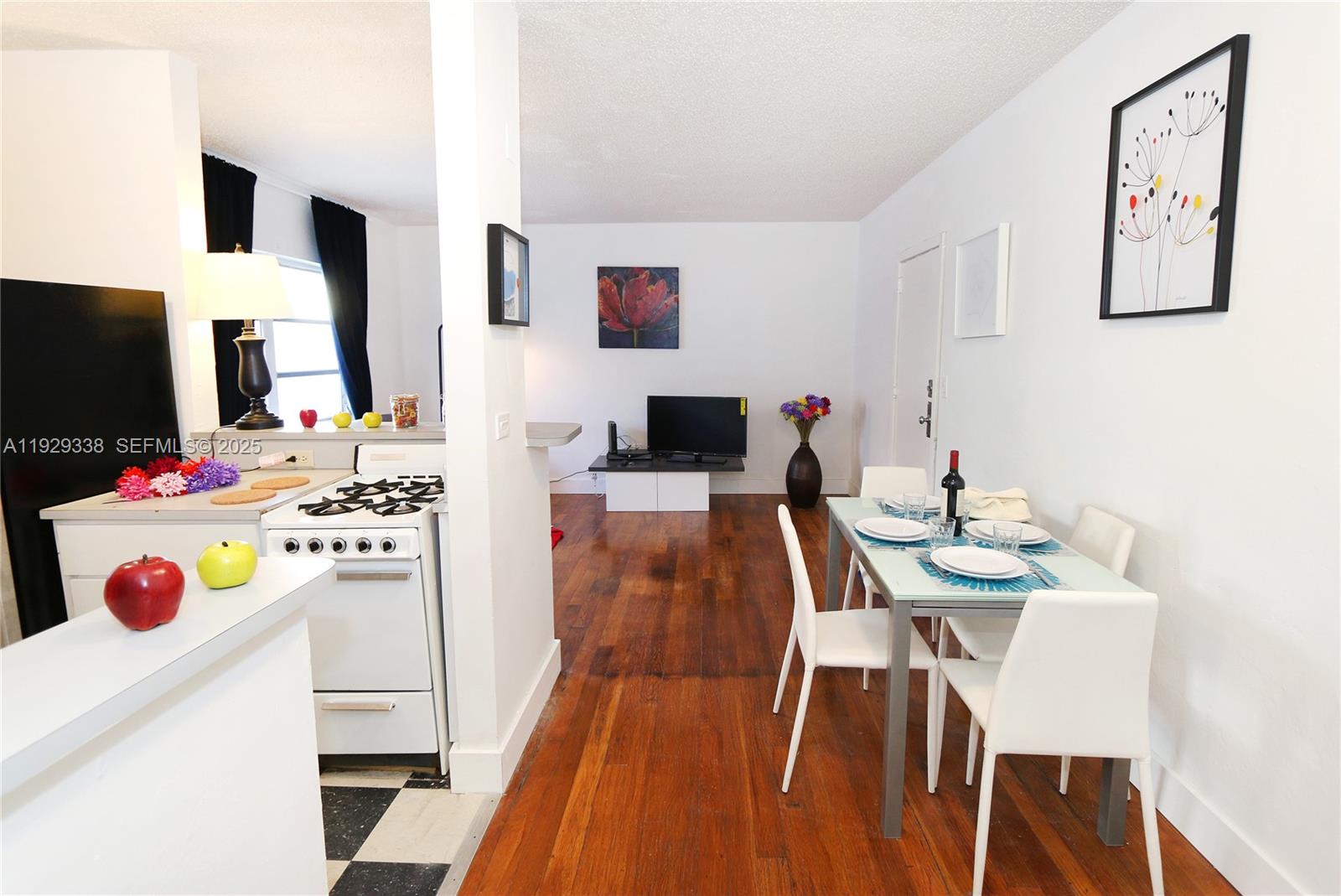 A dining area and kitchen feature white cabinets, hardwood floors, and a glass-top table — 807 Alton Rd, Miami Beach FL 33139, MIAMI BEACH, FL