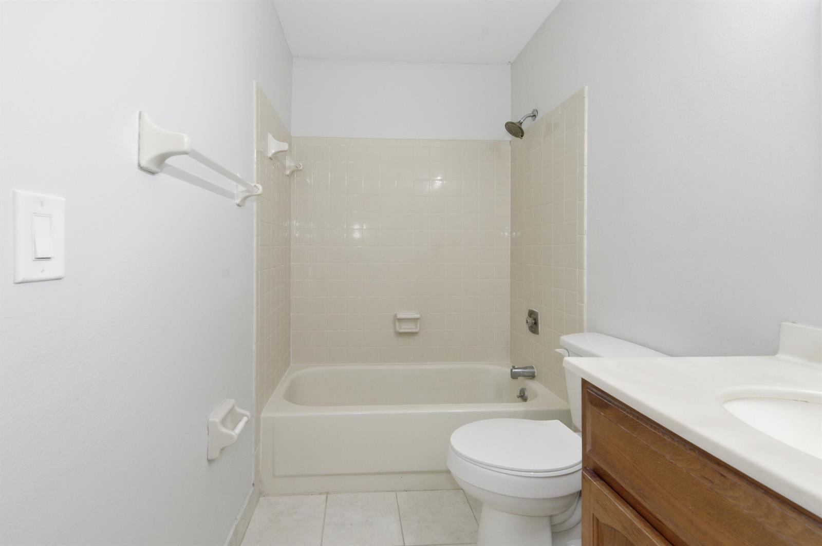 A bathroom features a beige tiled tub-shower combo, a white toilet, and a wood vanity — 729 NW 29th Avenue # D, Delray Beach FL 33445, DELRAY BEACH, FL