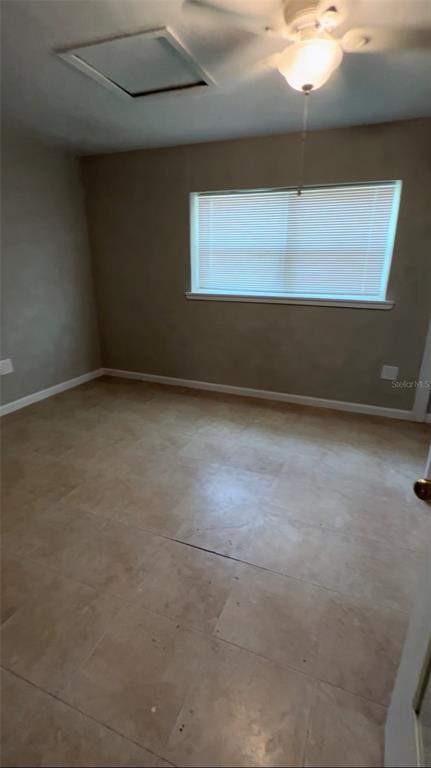 An empty bedroom features light-colored tile flooring, beige walls, a window with blinds, and a fan — 2618 LAKESHORE CIRCLE, PORT CHARLOTTE, FL