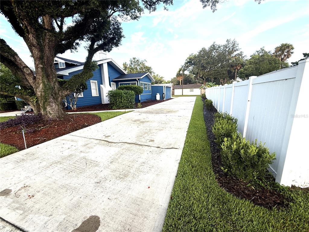 A long concrete driveway leads to a blue house with a large tree and fence — 1510 SANFORD AVE, SANFORD, FL
