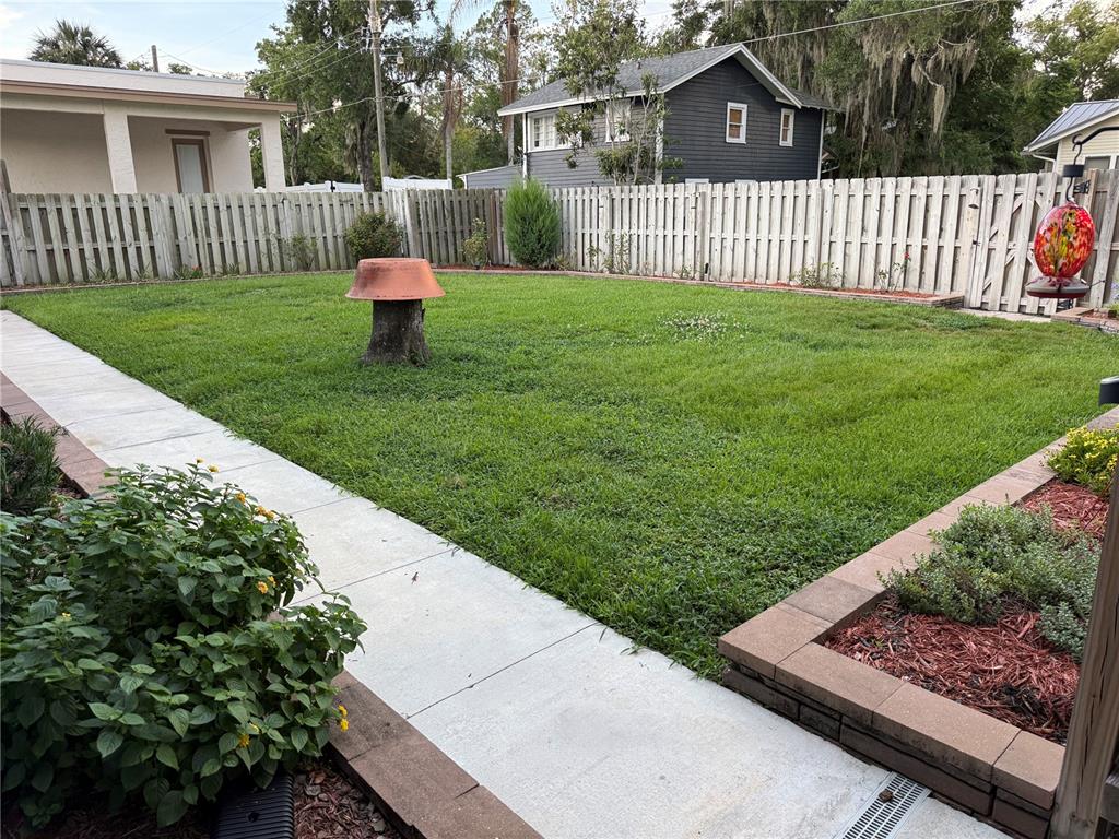 A fenced backyard features a green lawn, a concrete walkway, and a raised garden bed — 1510 SANFORD AVE, SANFORD, FL