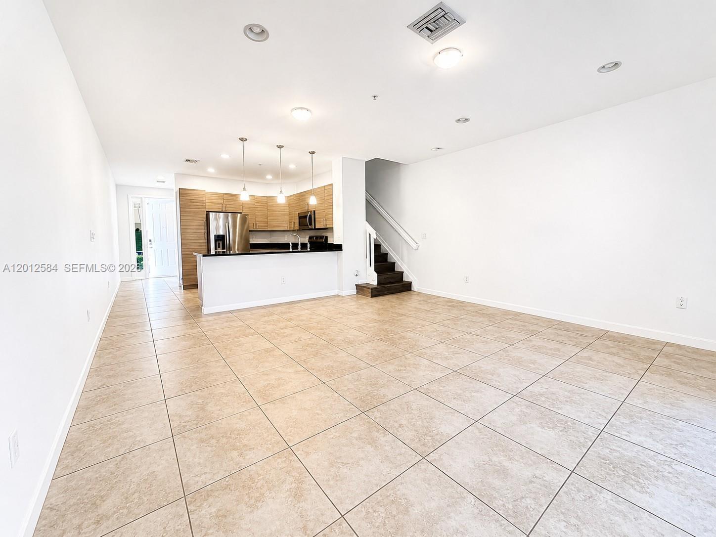 An open-concept living area features tile flooring, a kitchen with wood cabinets, and a staircase — 2574 SW 81st Ter # 2564, Miramar FL 33025, MIRAMAR, FL