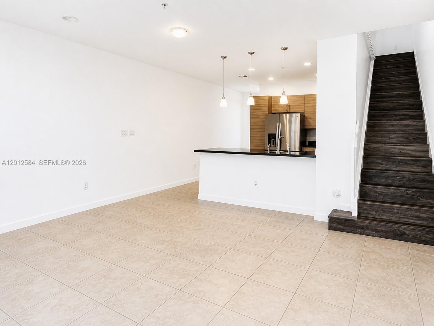 An open-concept kitchen with a breakfast bar overlooks a tiled living area and staircase — 2574 SW 81st Ter # 2564, Miramar FL 33025, MIRAMAR, FL