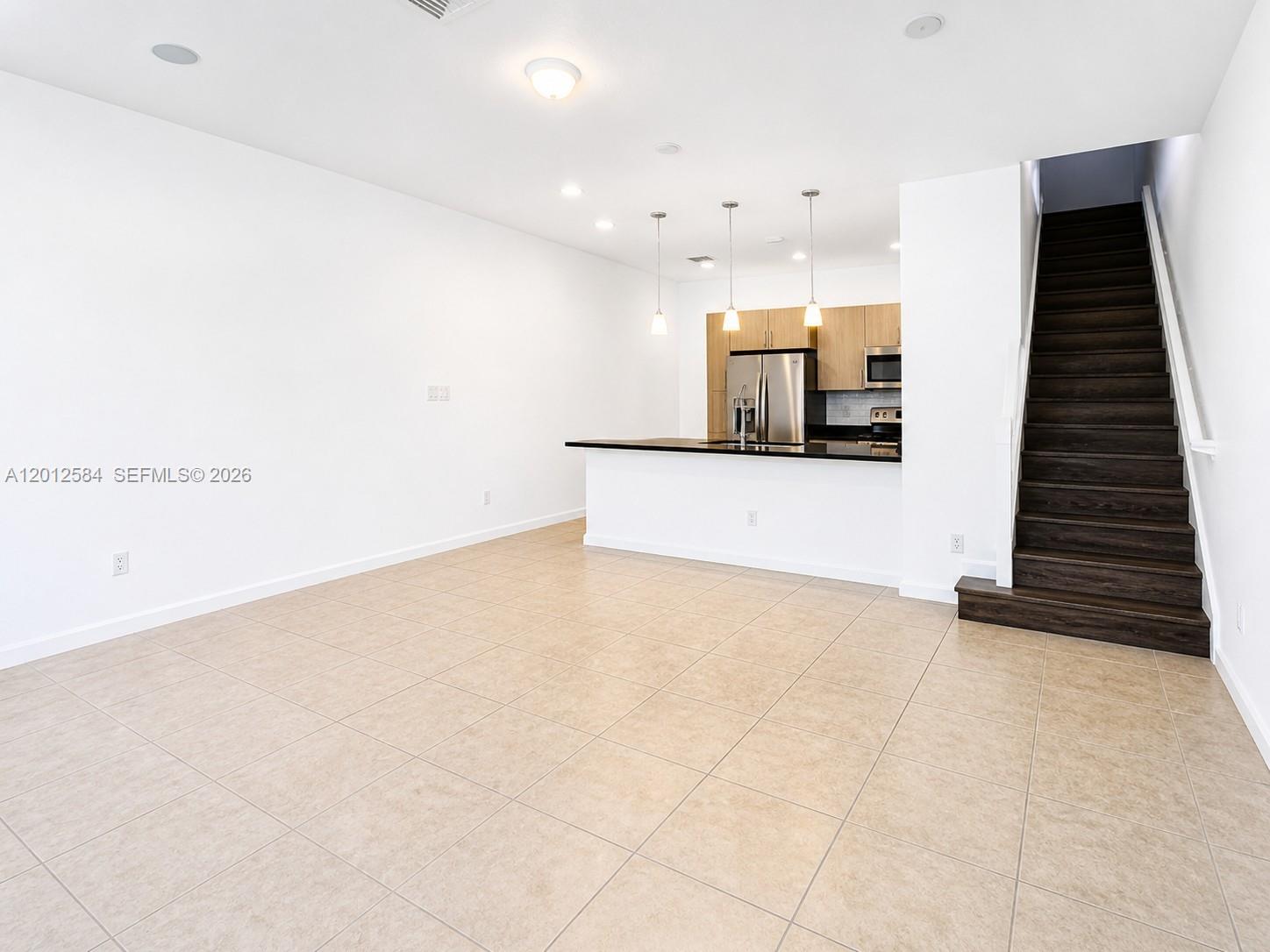 An open-concept living area features a kitchen with a breakfast bar and wooden stairs — 2574 SW 81st Ter # 2564, Miramar FL 33025, MIRAMAR, FL
