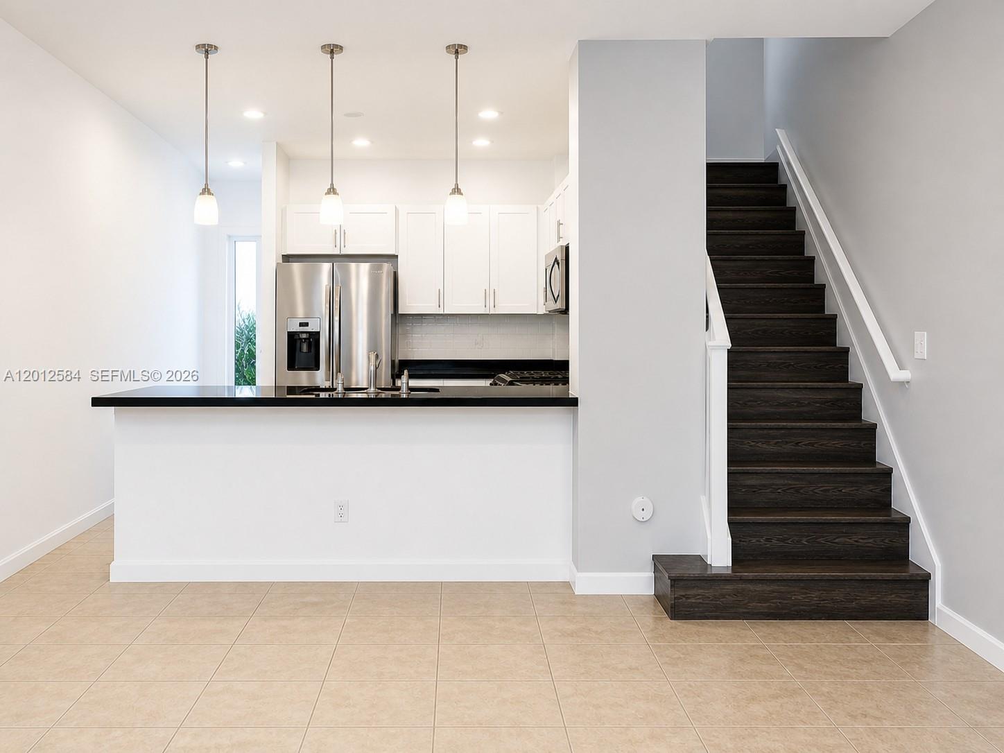 A kitchen with white cabinets and a black countertop sits beside a dark wooden staircase — 2574 SW 81st Ter # 2564, Miramar FL 33025, MIRAMAR, FL