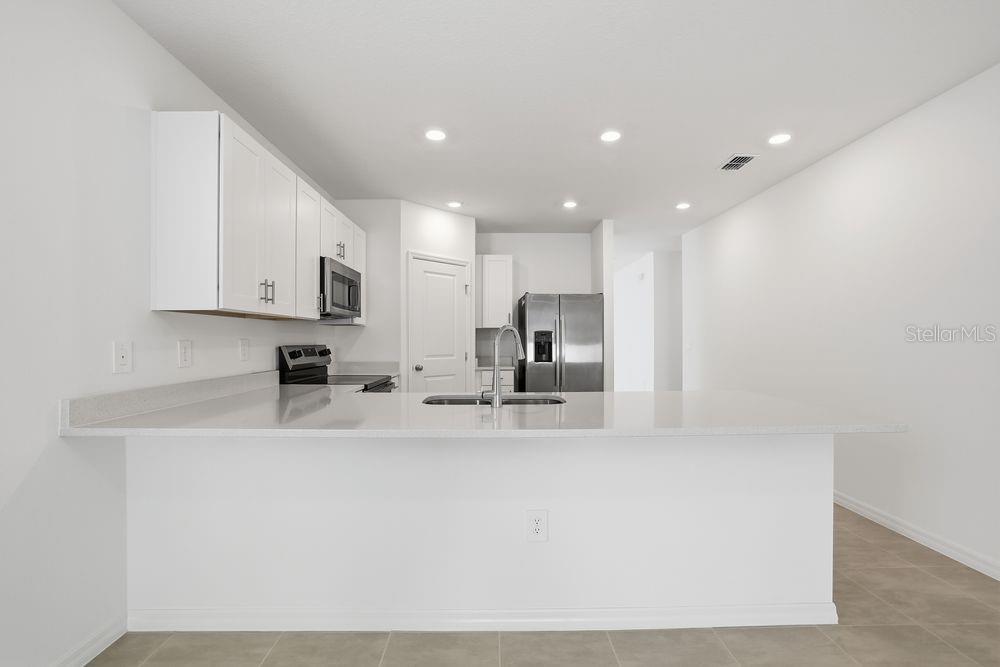 A modern kitchen features white cabinets, stainless steel appliances, and a large quartz island — 13502 TROPICAL BREEZE WAY, HUDSON, FL