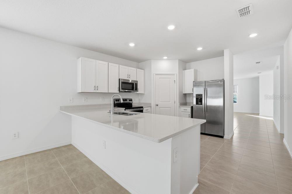 A modern kitchen features white cabinets, stainless steel appliances, and a large quartz island — 13502 TROPICAL BREEZE WAY, HUDSON, FL