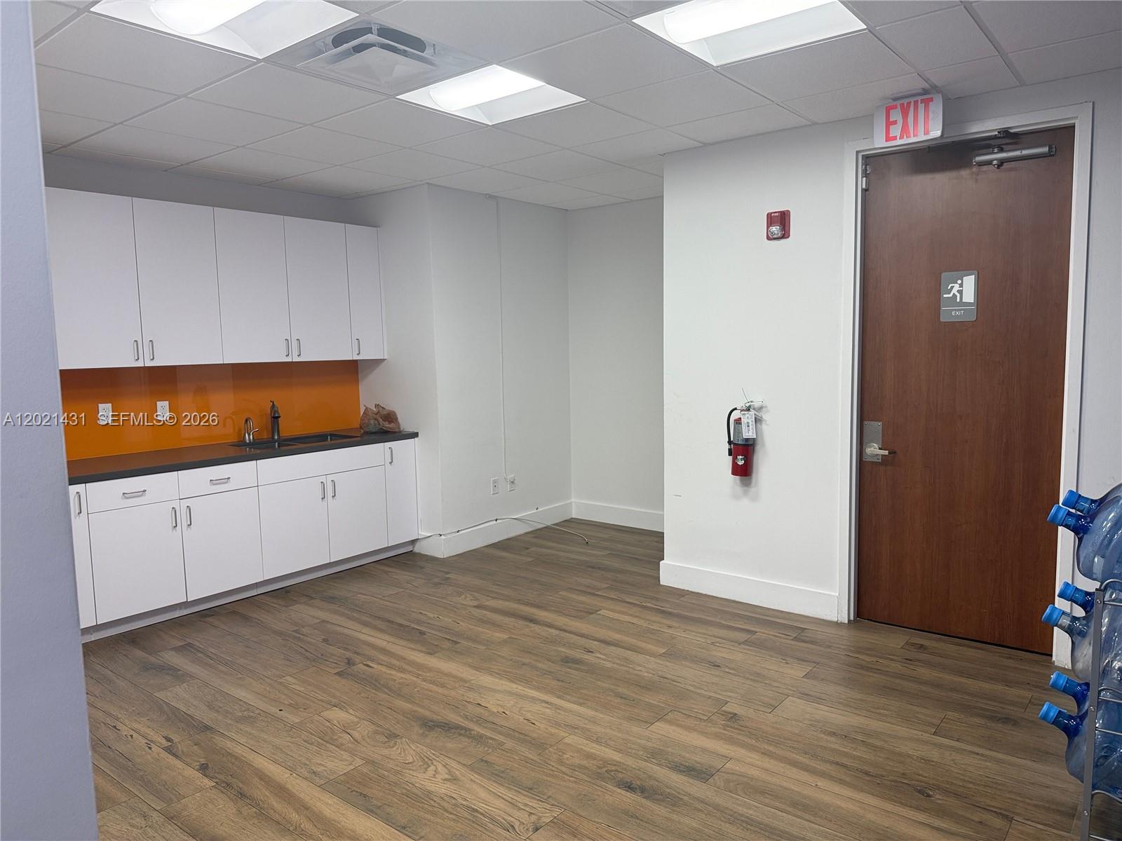 A breakroom features white cabinetry, an orange backsplash, wood-look flooring, and an exit door — 290 NW 165th St # 2, Miami FL 33169, MIAMI, FL