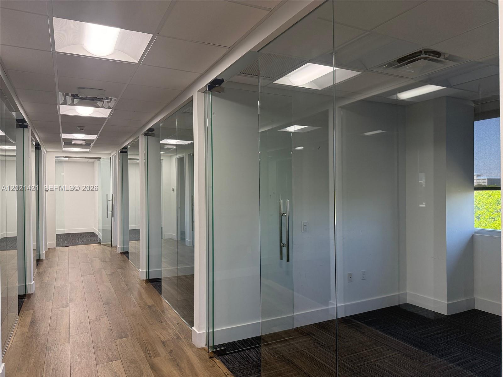 An office hallway features glass-walled rooms, wood-look flooring, and recessed ceiling lighting — 290 NW 165th St # 2, Miami FL 33169, MIAMI, FL