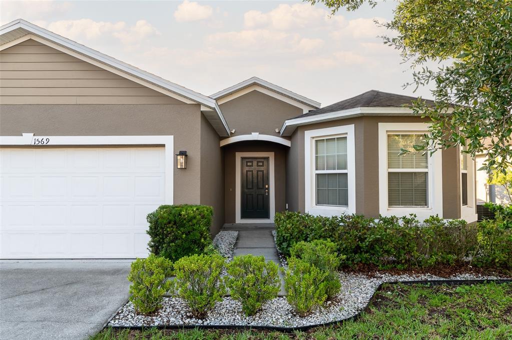 The exterior of a single-story house features a white garage door, dark door, and landscaping — 1569 TAMARIND ROAD, DAVENPORT, FL