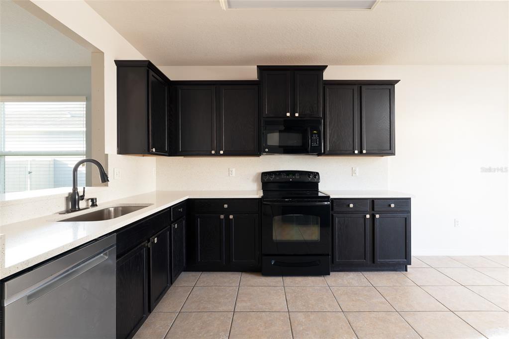 A kitchen features dark wood cabinets, white countertops, black appliances, and light-colored tile flooring — 1569 TAMARIND ROAD, DAVENPORT, FL