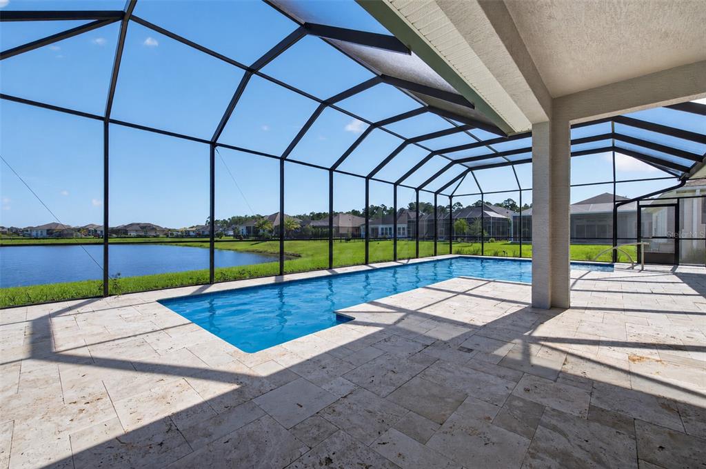A screened-in pool patio overlooks a lake at sunset with stone tile flooring — 305 AQUAMARINE WAY, DAYTONA BEACH, FL