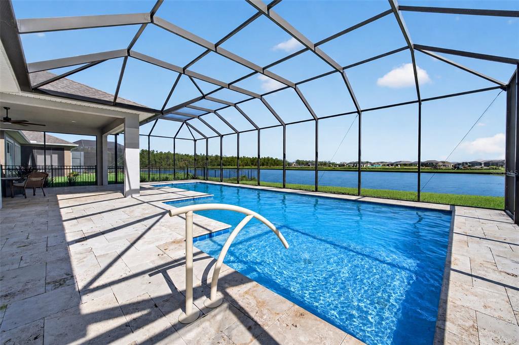 A screened-in patio features a rectangular swimming pool overlooking a lake and neighboring houses — 305 AQUAMARINE WAY, DAYTONA BEACH, FL