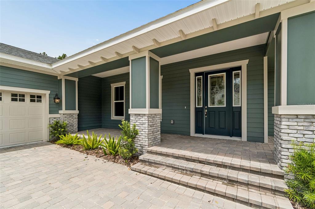 A teal-sided house exterior features a stone-accented porch, a paved driveway, and a dark door — 4881 MAJESTIC HILLS LOOP, BROOKSVILLE, FL