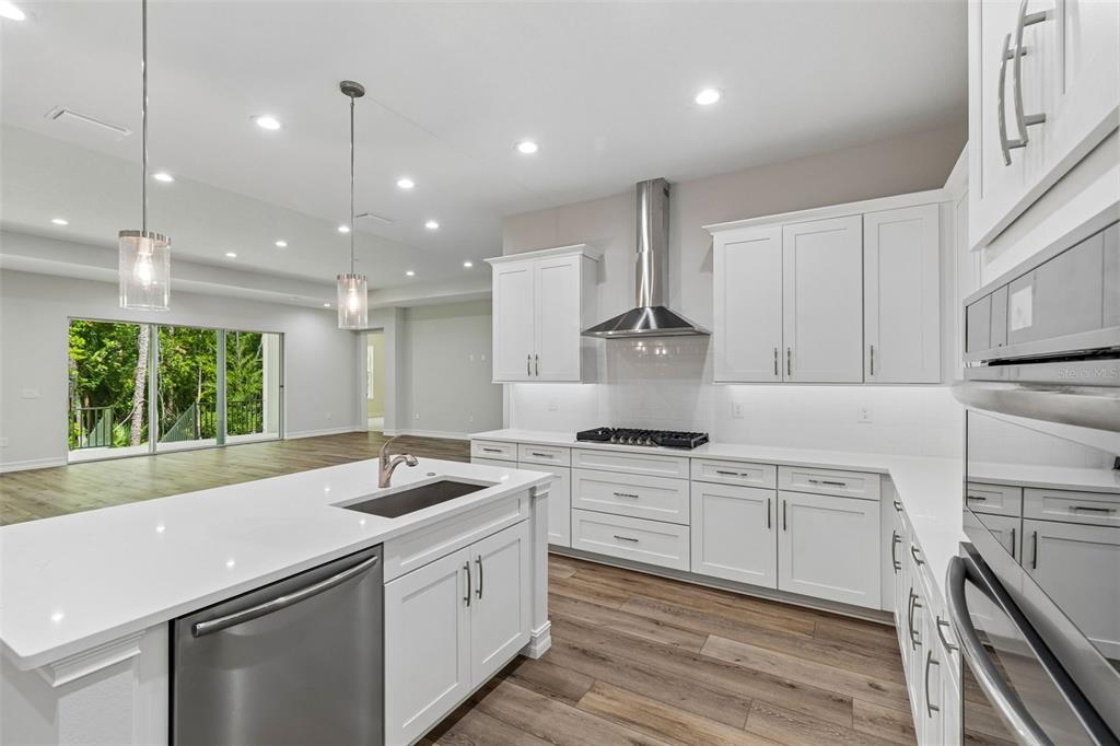 A modern white kitchen features a large island, stainless steel appliances, and wood-look flooring — 4881 MAJESTIC HILLS LOOP, BROOKSVILLE, FL