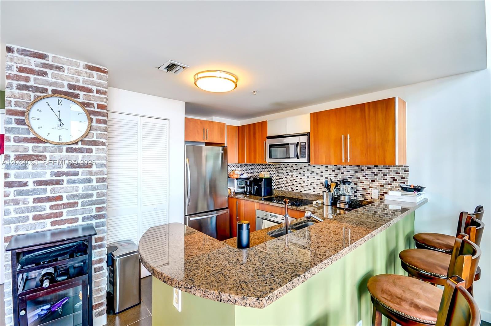 A kitchen features granite countertops, wood cabinets, stainless steel appliances, and a brick accent wall — 300 S Biscayne Bluv # 1022, Miami FL 33131, MIAMI, FL