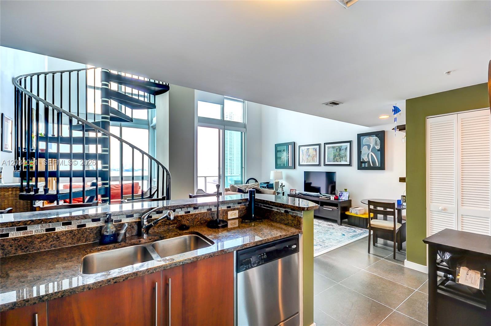 A kitchen with granite countertops overlooks a living area featuring a spiral staircase and windows — 300 S Biscayne Bluv # 1022, Miami FL 33131, MIAMI, FL