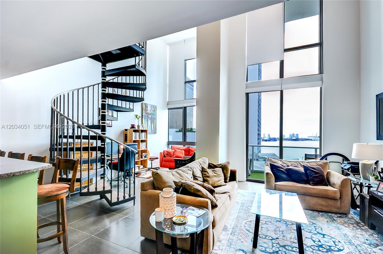 A living room features a spiral staircase, floor-to-ceiling windows, and a view of the water — 300 S Biscayne Bluv # 1022, Miami FL 33131, MIAMI, FL