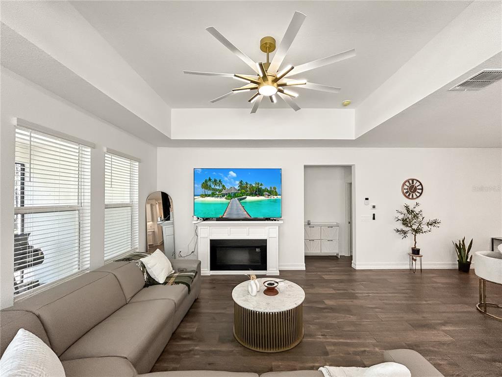 A living room features a grey sofa, a fireplace with a television, and a ceiling fan — 18334 SERENE LAKE LOOP, LUTZ, FL