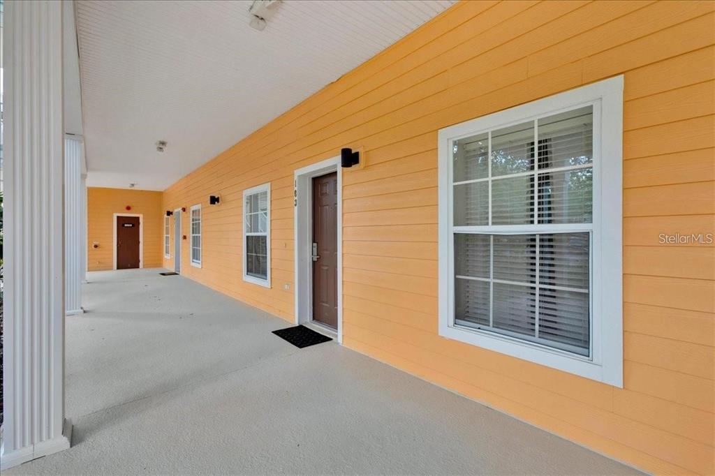 A long, covered porch with orange siding, multiple brown doors, and white-trimmed windows — 103 ROGUES RETREAT UNIT 22-103, DAVENPORT, FL