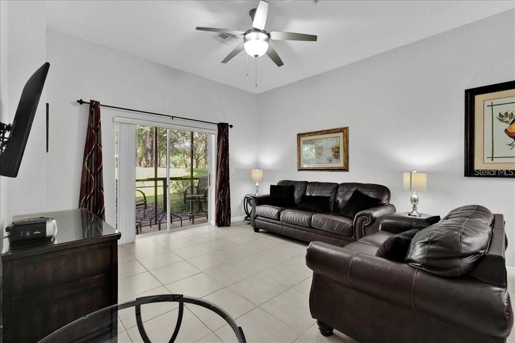 A living room features tile flooring, two dark leather sofas, and a sliding glass door — 103 ROGUES RETREAT UNIT 22-103, DAVENPORT, FL