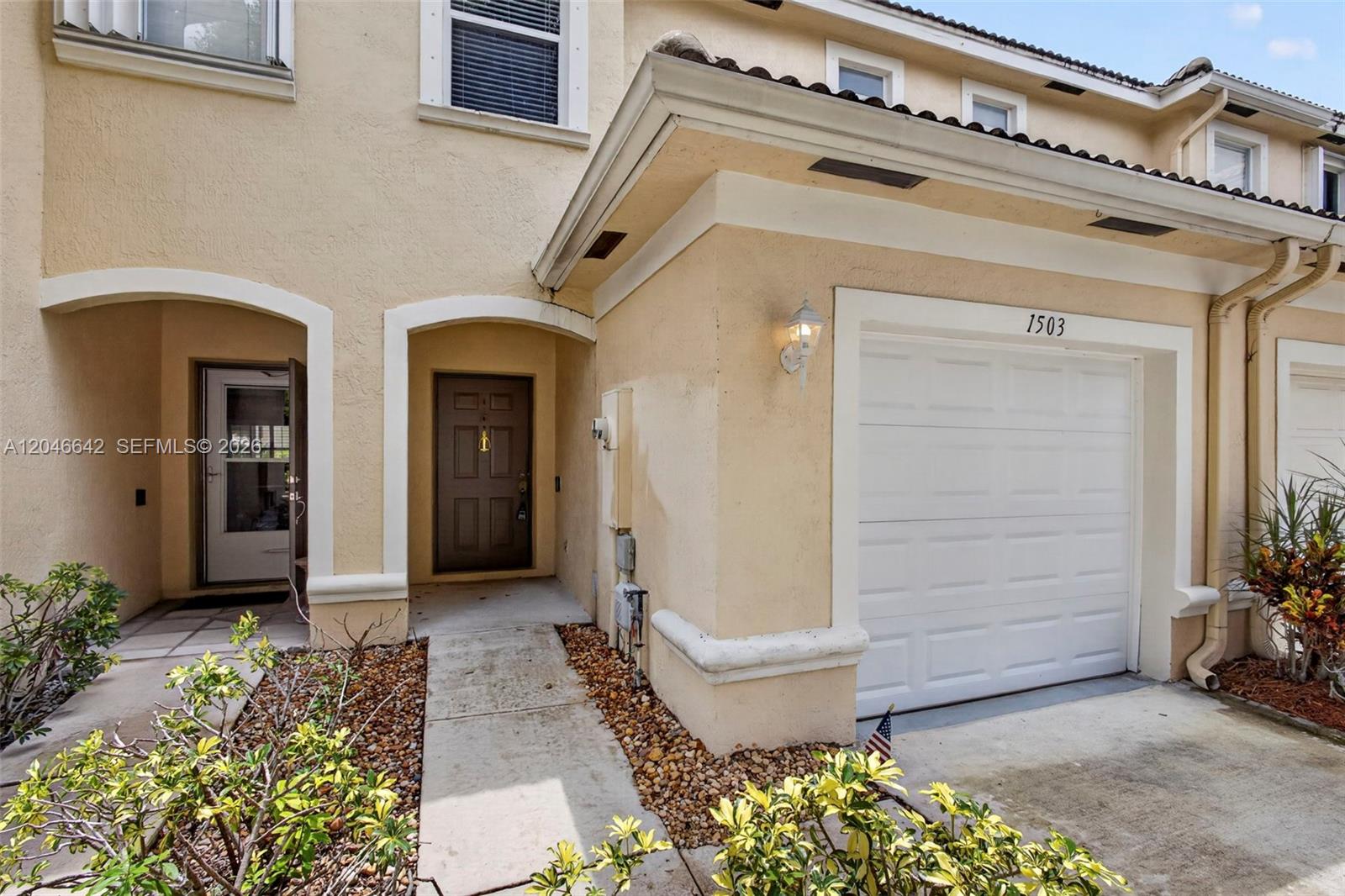 The exterior of a two-story townhouse features a tan stucco facade, a garage, and an entryway — 1503 New Castle Ter, Wellington FL 33414, WELLINGTON, FL