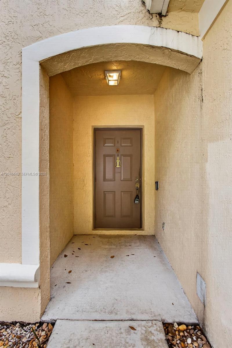 A brown front door is recessed within a stucco entryway featuring a ceiling light fixture — 1503 New Castle Ter, Wellington FL 33414, WELLINGTON, FL