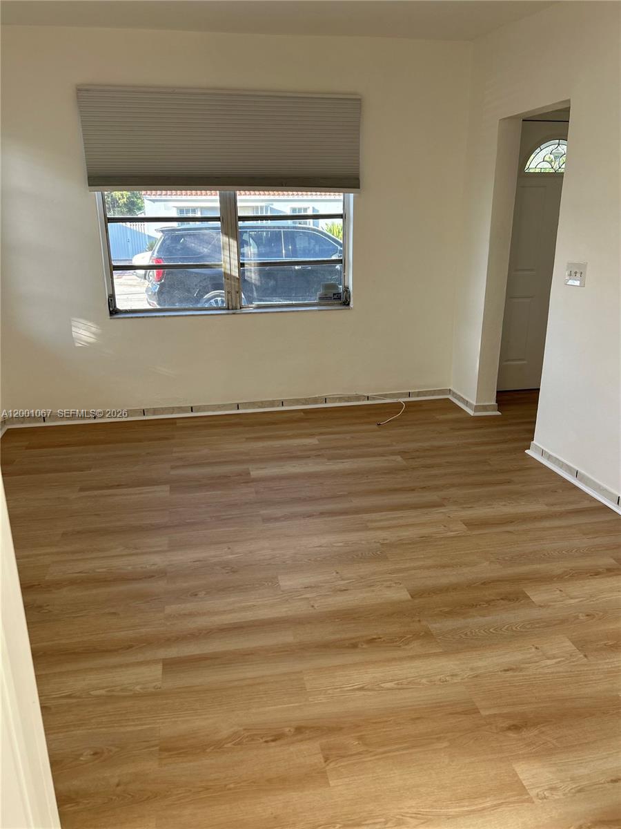 An empty room features light wood-look flooring, beige walls, and a window with a blind — MIAMI, FL